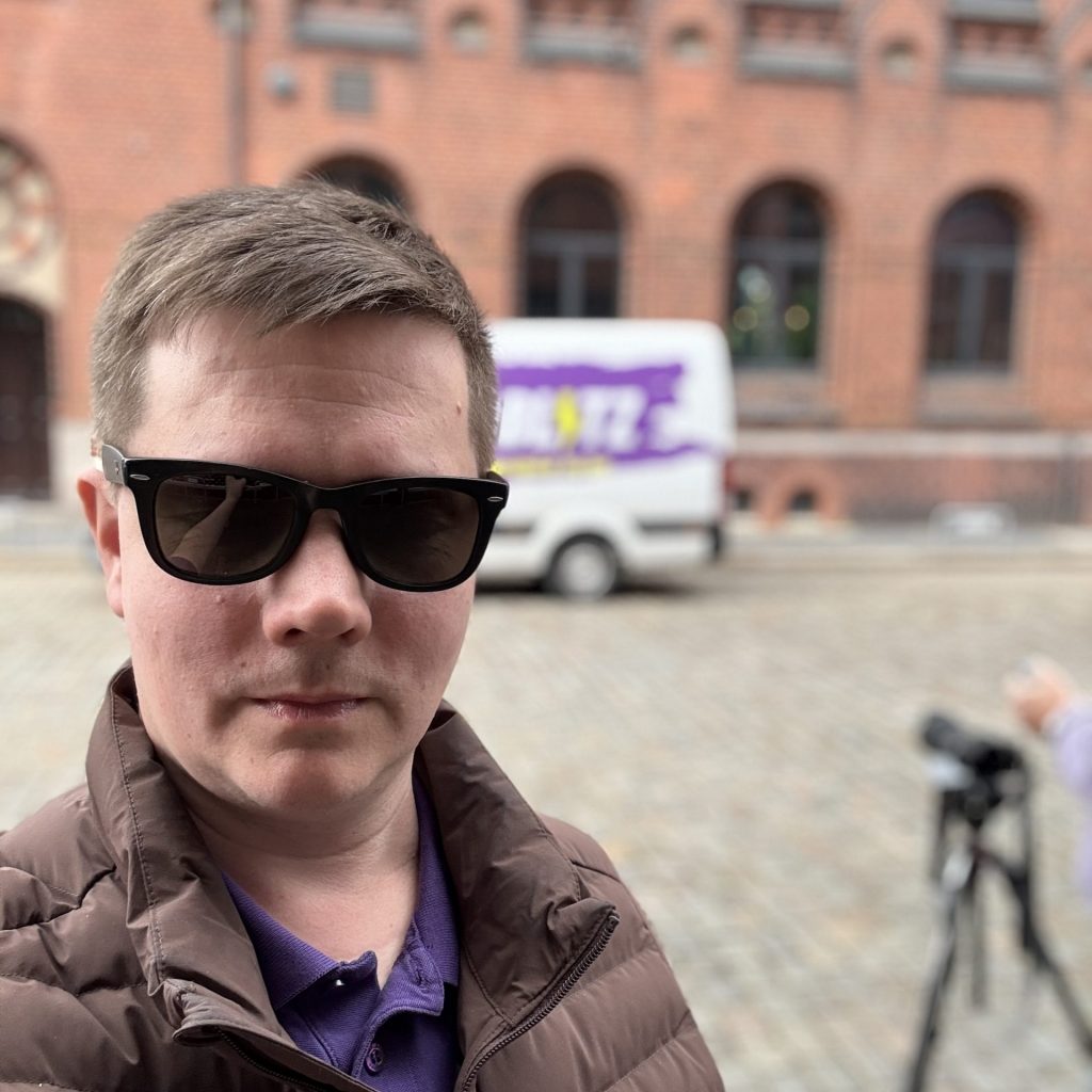 Person vor einem Backsteinhaus. Im Hintergrund ein Transporter